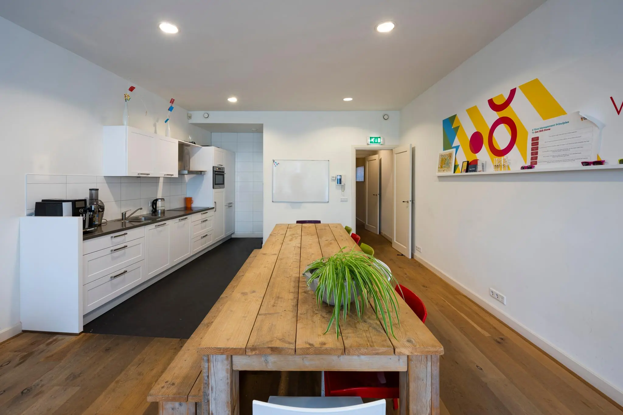 Moderne gemeenschappelijke keuken met lange houten eettafel en kleurrijke wanddecoratie aan de Nieuwezijds Voorburgwal.